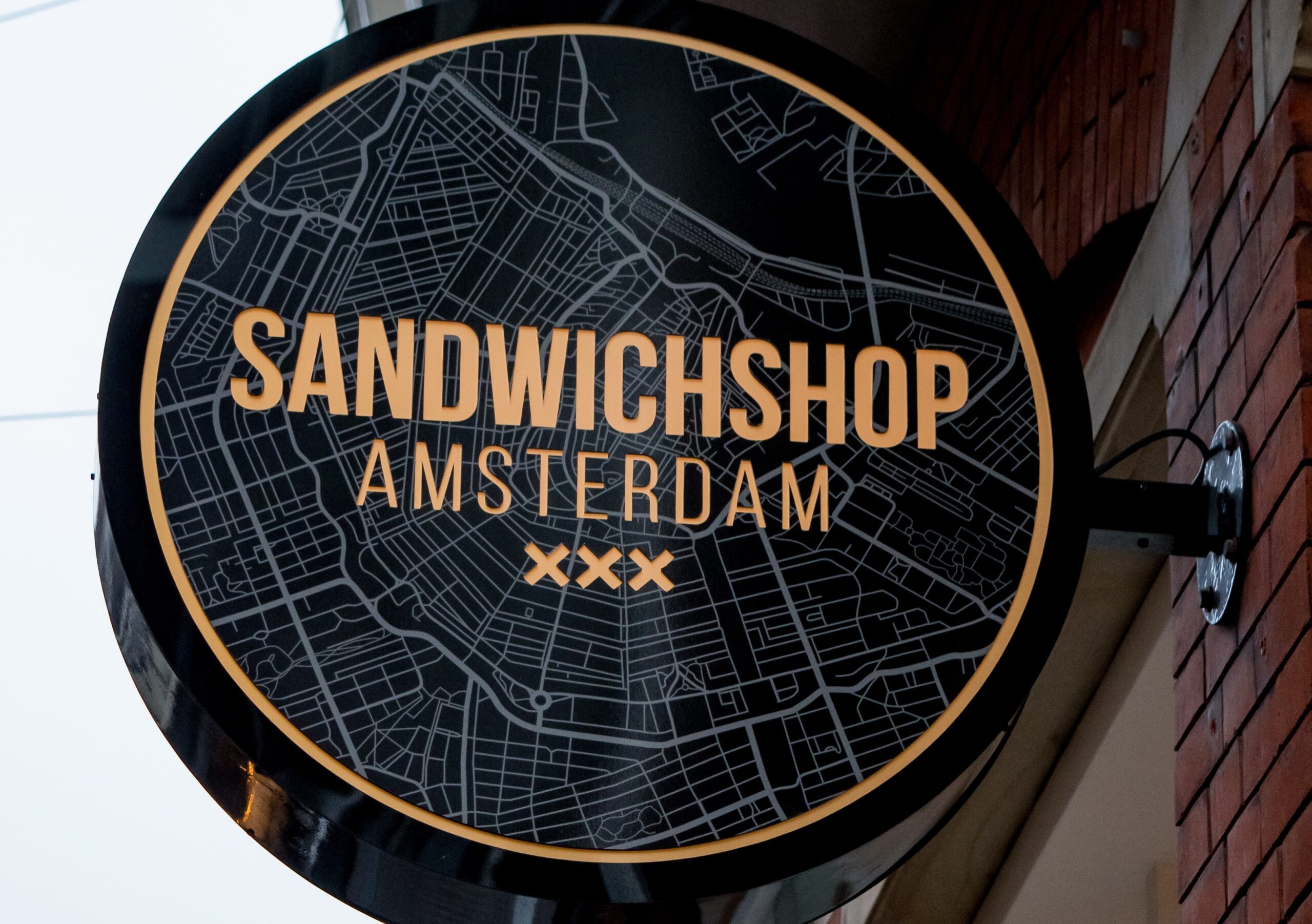 Afbeelding van het logo van de Sandwichshop op een bord aan de buitenzijde van de zaak in hartje Amsterdam!